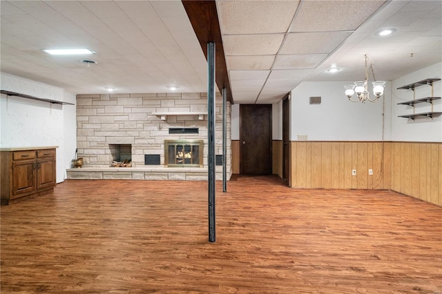 living room with a paneled ceiling, wooden walls, light wood-type flooring, a fireplace, and a notable chandelier