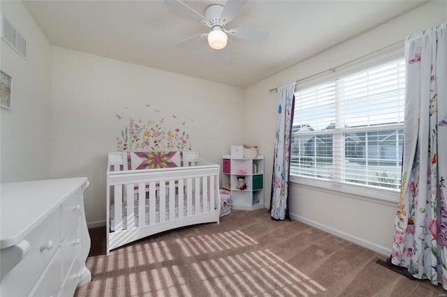 carpeted bedroom featuring a nursery area and ceiling fan