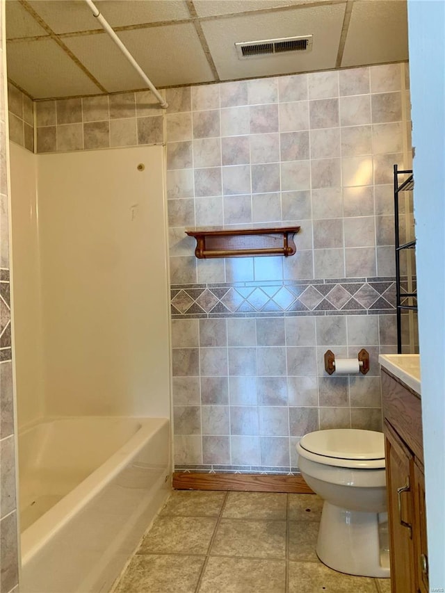 full bathroom featuring a paneled ceiling, vanity, tile patterned floors, toilet, and tile walls