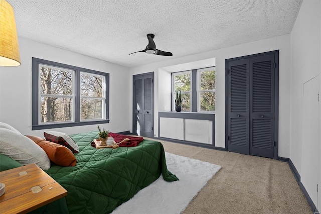 carpeted bedroom with a textured ceiling, multiple closets, ceiling fan, and multiple windows