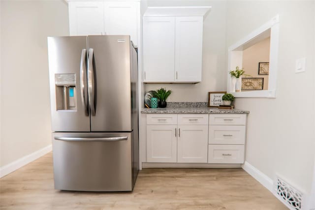 kitchen with light stone counters, light wood-type flooring, white cabinetry, and stainless steel refrigerator with ice dispenser