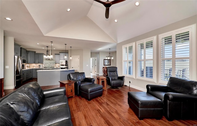 living room with high vaulted ceiling, ceiling fan with notable chandelier, recessed lighting, baseboards, and dark wood-style flooring