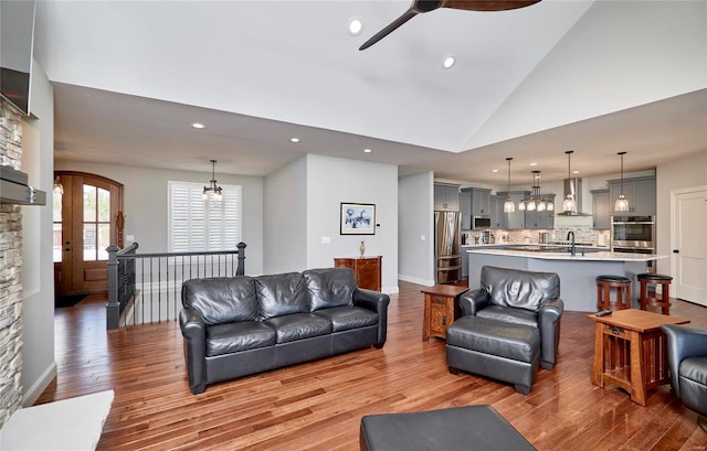 living area featuring baseboards, high vaulted ceiling, recessed lighting, ceiling fan, and light wood-style floors