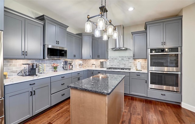 kitchen with gray cabinets, dark stone countertops, stainless steel appliances, wall chimney range hood, and dark wood-style flooring