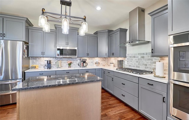 kitchen with dark stone countertops, stainless steel appliances, gray cabinets, and wall chimney range hood