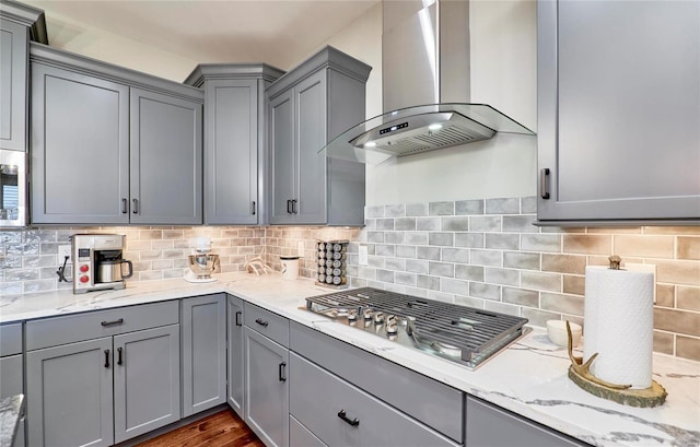 kitchen with wall chimney exhaust hood, gray cabinets, backsplash, and stainless steel appliances