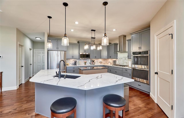 kitchen with a sink, stainless steel appliances, wall chimney exhaust hood, and gray cabinets