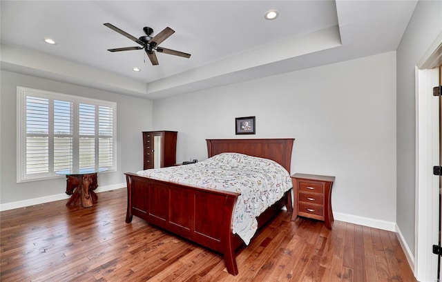 bedroom featuring a tray ceiling, baseboards, and hardwood / wood-style flooring