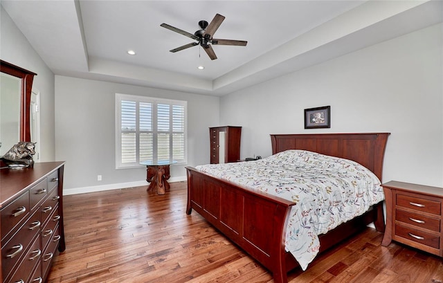 bedroom featuring a raised ceiling, recessed lighting, wood finished floors, and baseboards