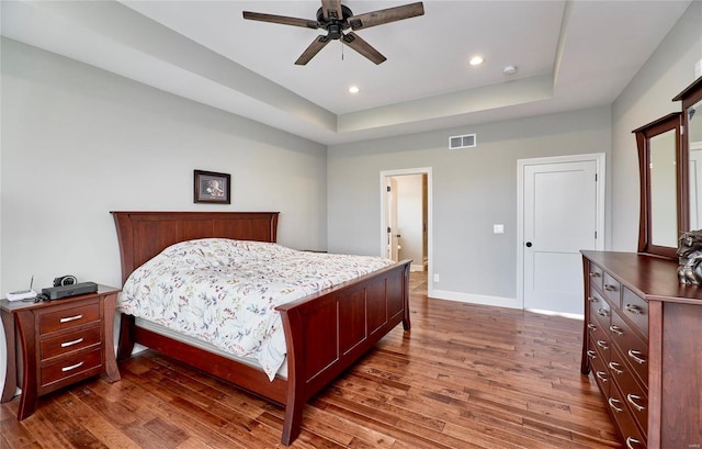 bedroom with visible vents, a raised ceiling, dark wood finished floors, recessed lighting, and baseboards