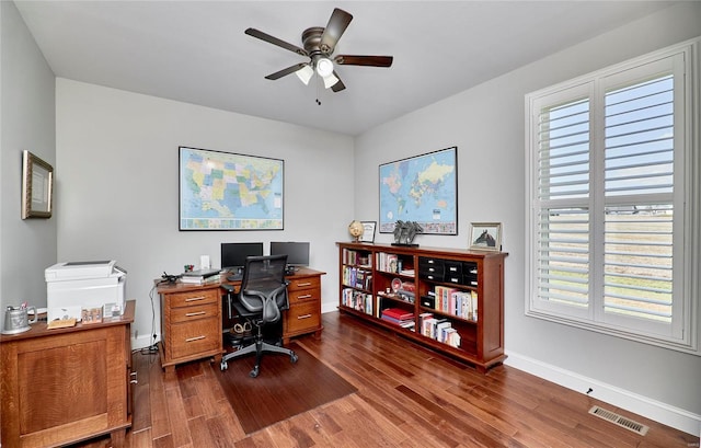 home office with a ceiling fan, dark wood-style floors, visible vents, and baseboards