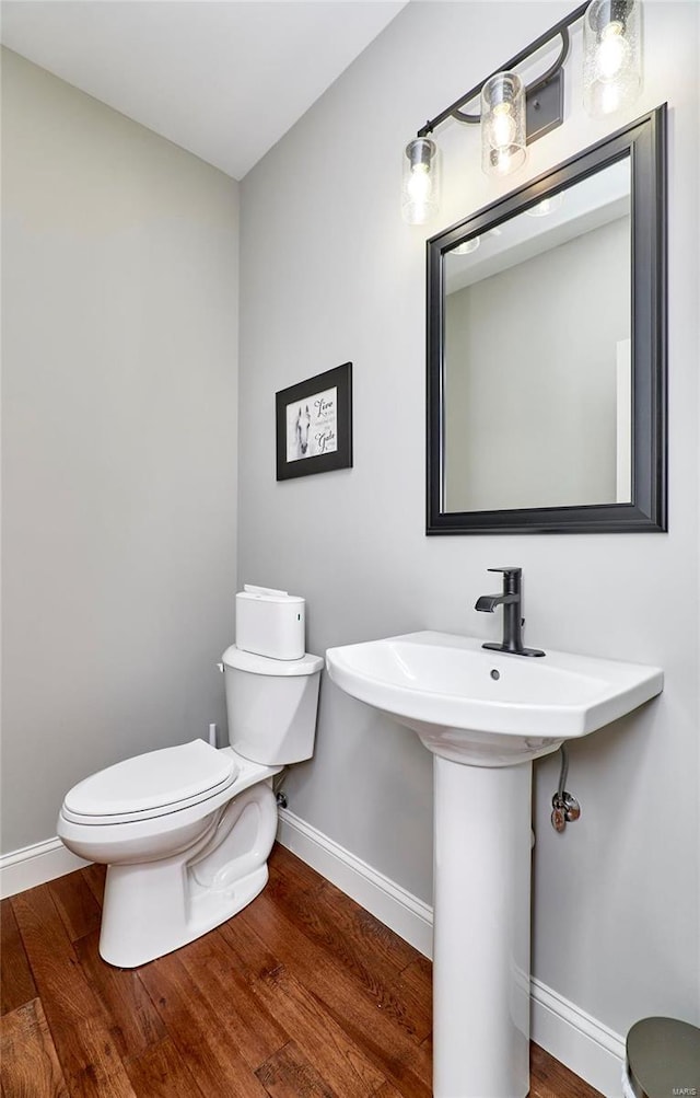 half bathroom with toilet, wood finished floors, and baseboards