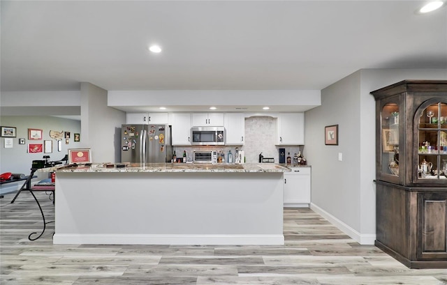 kitchen with light wood-type flooring, backsplash, appliances with stainless steel finishes, white cabinets, and light stone countertops