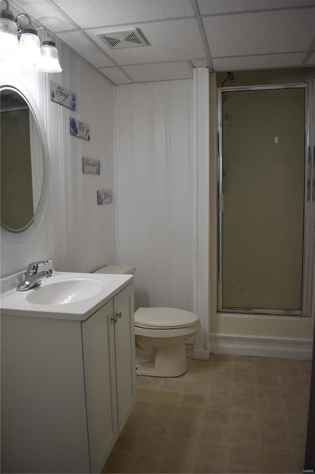 bathroom featuring a drop ceiling, toilet, walk in shower, and vanity