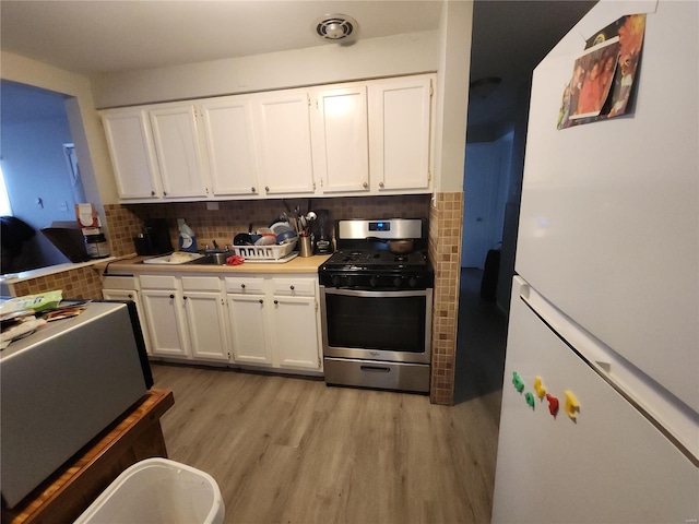 kitchen with light countertops, freestanding refrigerator, white cabinets, stainless steel range with gas stovetop, and light wood-type flooring