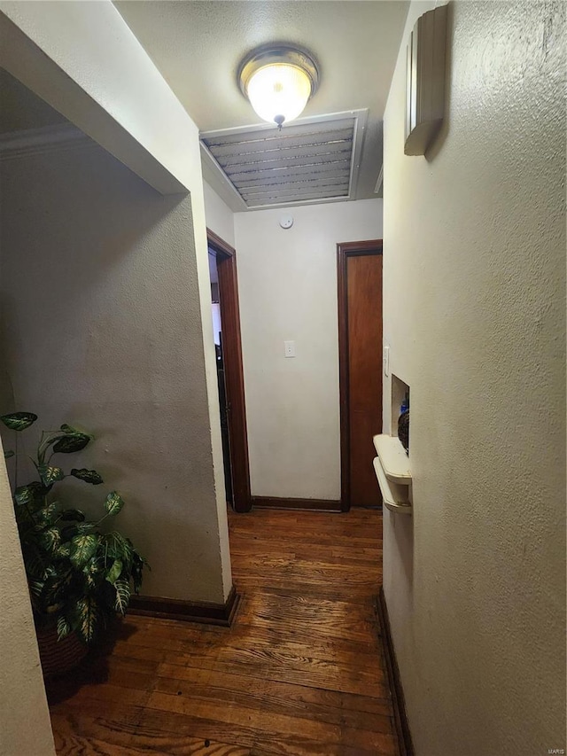 hallway with a textured wall, dark wood finished floors, and baseboards