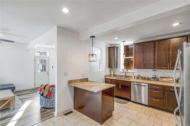 kitchen featuring light stone countertops, sink, stainless steel appliances, kitchen peninsula, and decorative light fixtures