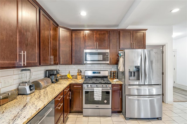 kitchen with light stone countertops, backsplash, stainless steel appliances, and light tile patterned flooring