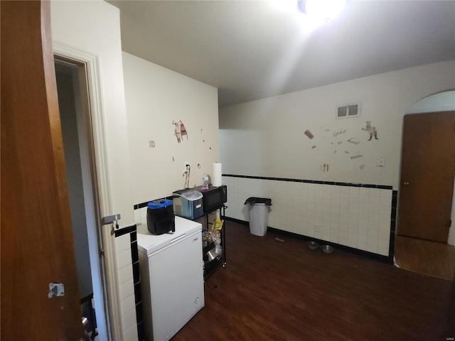 interior space with a wainscoted wall, visible vents, tile walls, light countertops, and dark wood finished floors