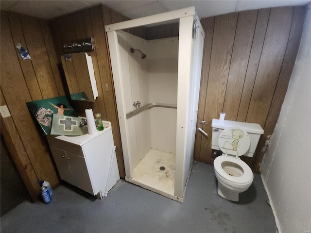 bathroom featuring concrete flooring, toilet, wooden walls, vanity, and a stall shower