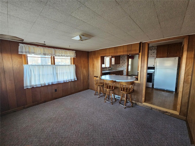 kitchen with wooden walls, carpet floors, a healthy amount of sunlight, and white appliances