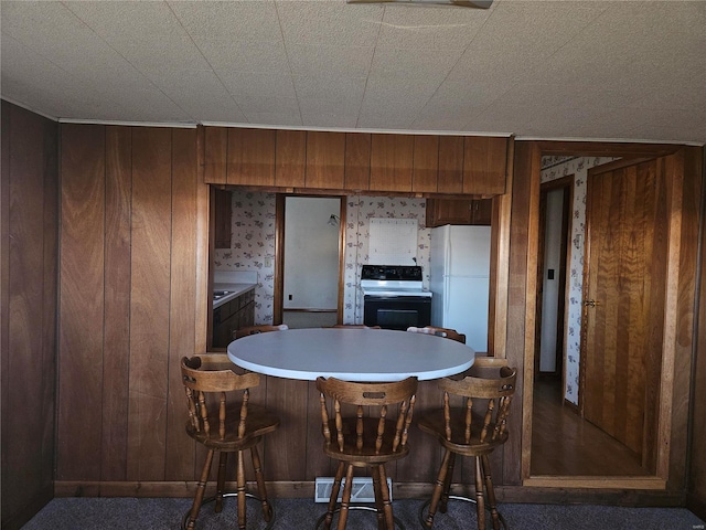 kitchen with dark carpet, white fridge, black electric range oven, and wood walls