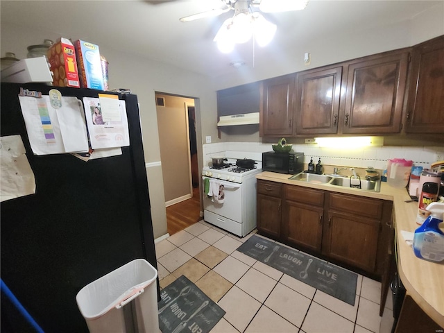 kitchen featuring light tile patterned floors, under cabinet range hood, a sink, light countertops, and black appliances