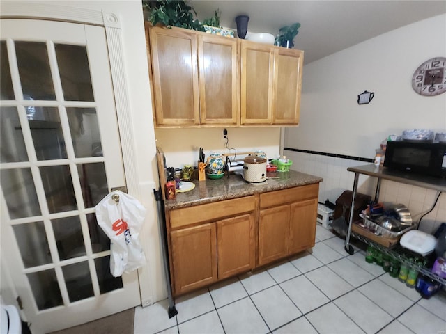 kitchen featuring tile walls, dark countertops, wainscoting, light tile patterned flooring, and black microwave