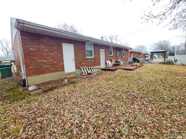 rear view of property featuring entry steps, brick siding, fence, a gazebo, and a wooden deck