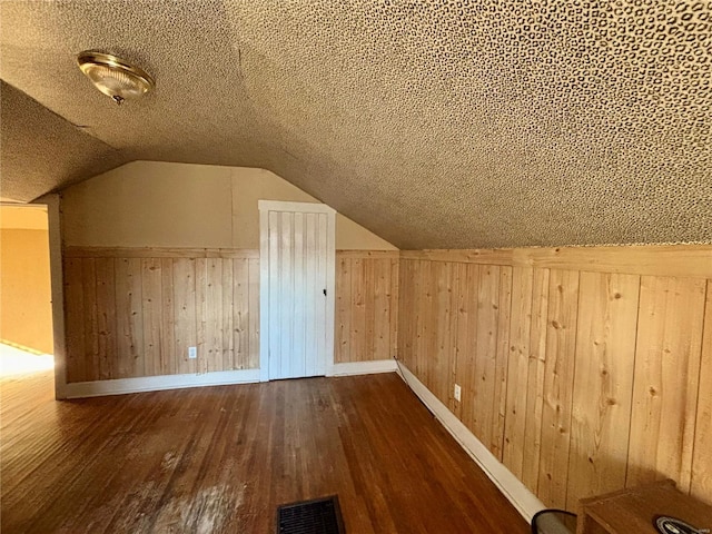 bonus room featuring a textured ceiling, wood walls, dark hardwood / wood-style flooring, and vaulted ceiling