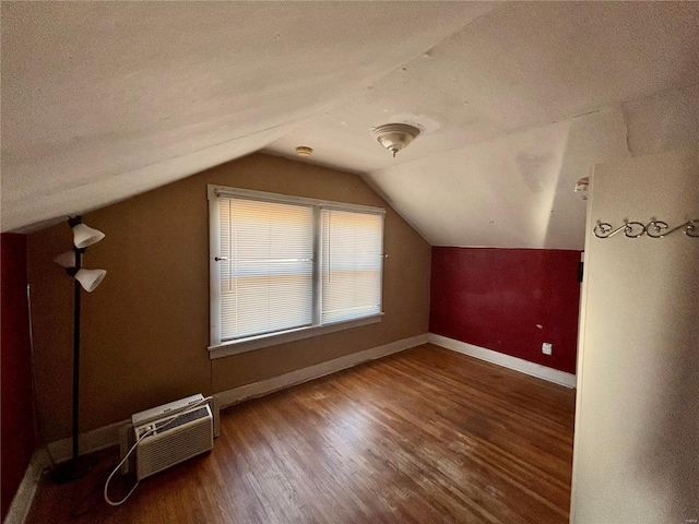 additional living space featuring dark hardwood / wood-style flooring, a wall unit AC, and vaulted ceiling