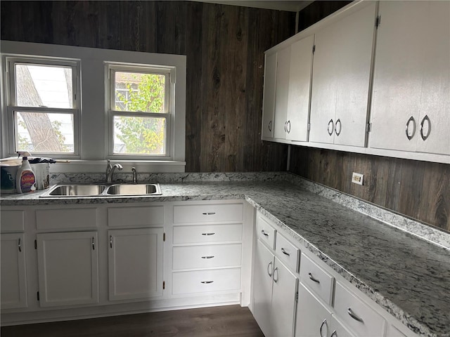 kitchen featuring white cabinets, wood walls, sink, and dark wood-type flooring