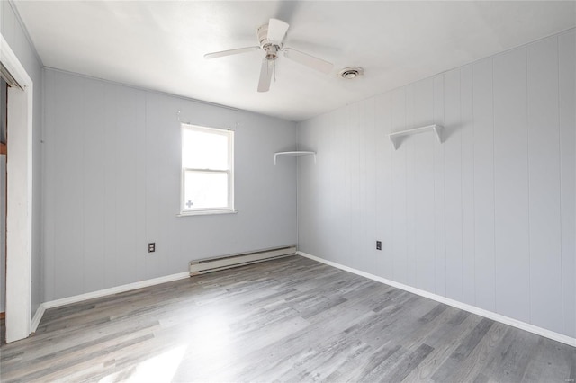 unfurnished room featuring wooden walls, light hardwood / wood-style floors, ceiling fan, and a baseboard heating unit