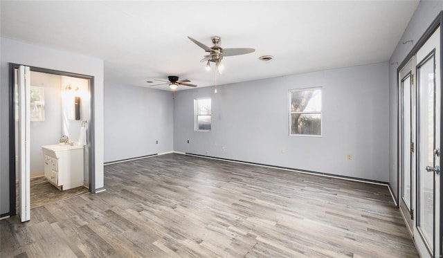 unfurnished bedroom featuring ceiling fan, light hardwood / wood-style floors, connected bathroom, and multiple windows