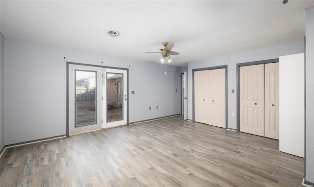 unfurnished bedroom featuring ceiling fan, light hardwood / wood-style floors, and two closets