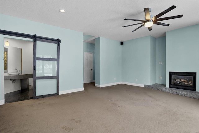 unfurnished living room featuring a textured ceiling, a barn door, ceiling fan, dark carpet, and sink