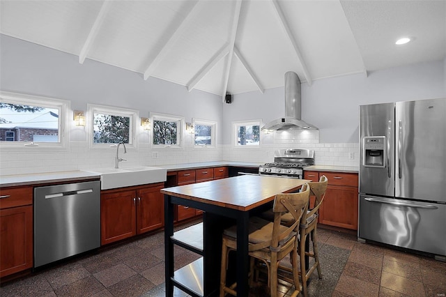 kitchen with appliances with stainless steel finishes, lofted ceiling with beams, sink, wall chimney range hood, and tasteful backsplash