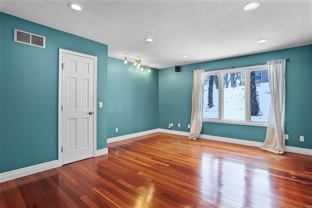 spare room featuring a textured ceiling, rail lighting, and wood-type flooring