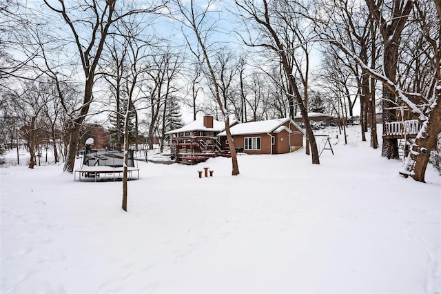 snowy yard featuring a wooden deck and a trampoline