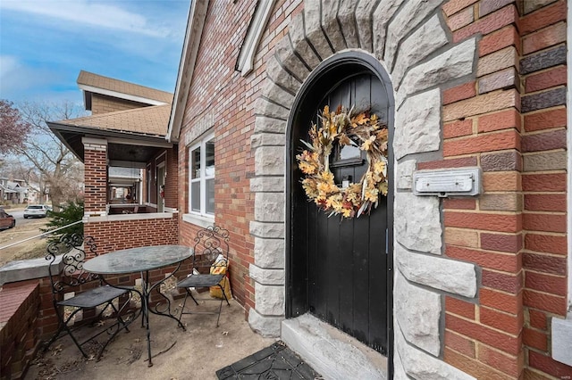 doorway to property featuring brick siding and a shingled roof