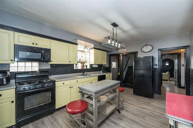 kitchen with tasteful backsplash, light wood-style floors, light countertops, black appliances, and pendant lighting