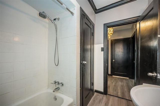 full bath with tile walls, washtub / shower combination, ornamental molding, a sink, and wood finished floors