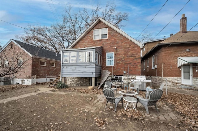 rear view of house featuring an outdoor fire pit, brick siding, and fence