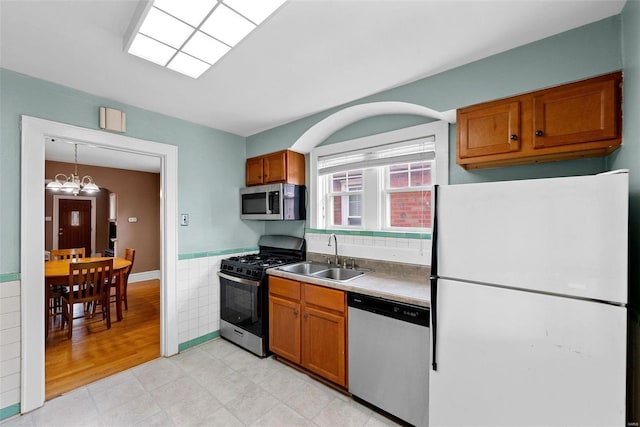 kitchen featuring stainless steel appliances, a notable chandelier, tile walls, hanging light fixtures, and sink