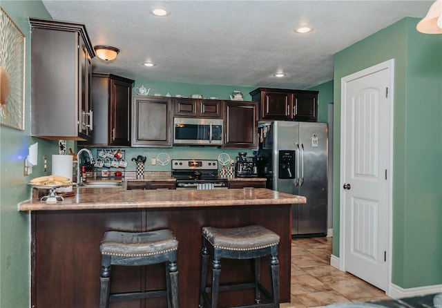 kitchen featuring sink, dark brown cabinets, stainless steel appliances, a textured ceiling, and light tile patterned flooring