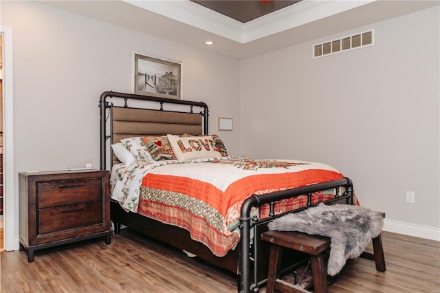 bedroom with crown molding, hardwood / wood-style flooring, and a raised ceiling