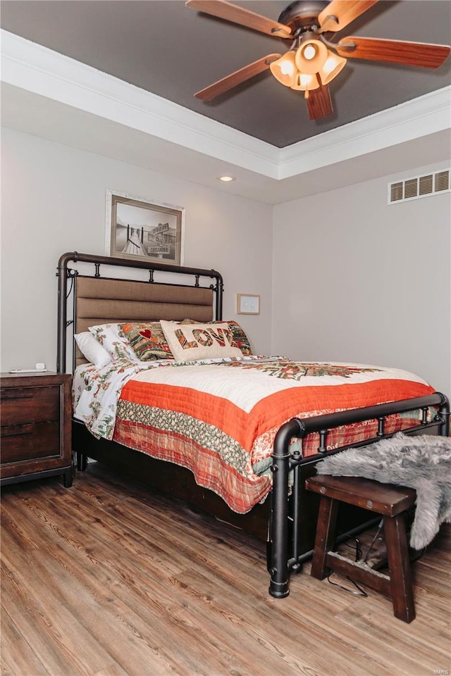 bedroom with crown molding, ceiling fan, a tray ceiling, and hardwood / wood-style flooring