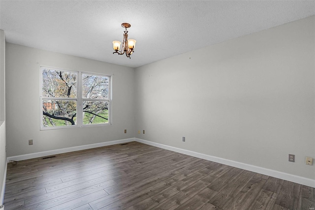 empty room with dark wood-type flooring, a textured ceiling, and a notable chandelier