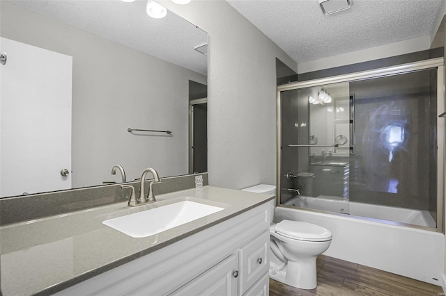 full bathroom with bath / shower combo with glass door, vanity, a textured ceiling, hardwood / wood-style floors, and toilet