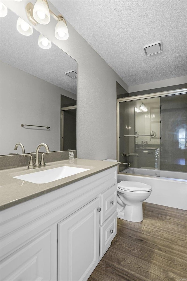 full bathroom with wood-type flooring, a textured ceiling, toilet, shower / bath combination with glass door, and vanity